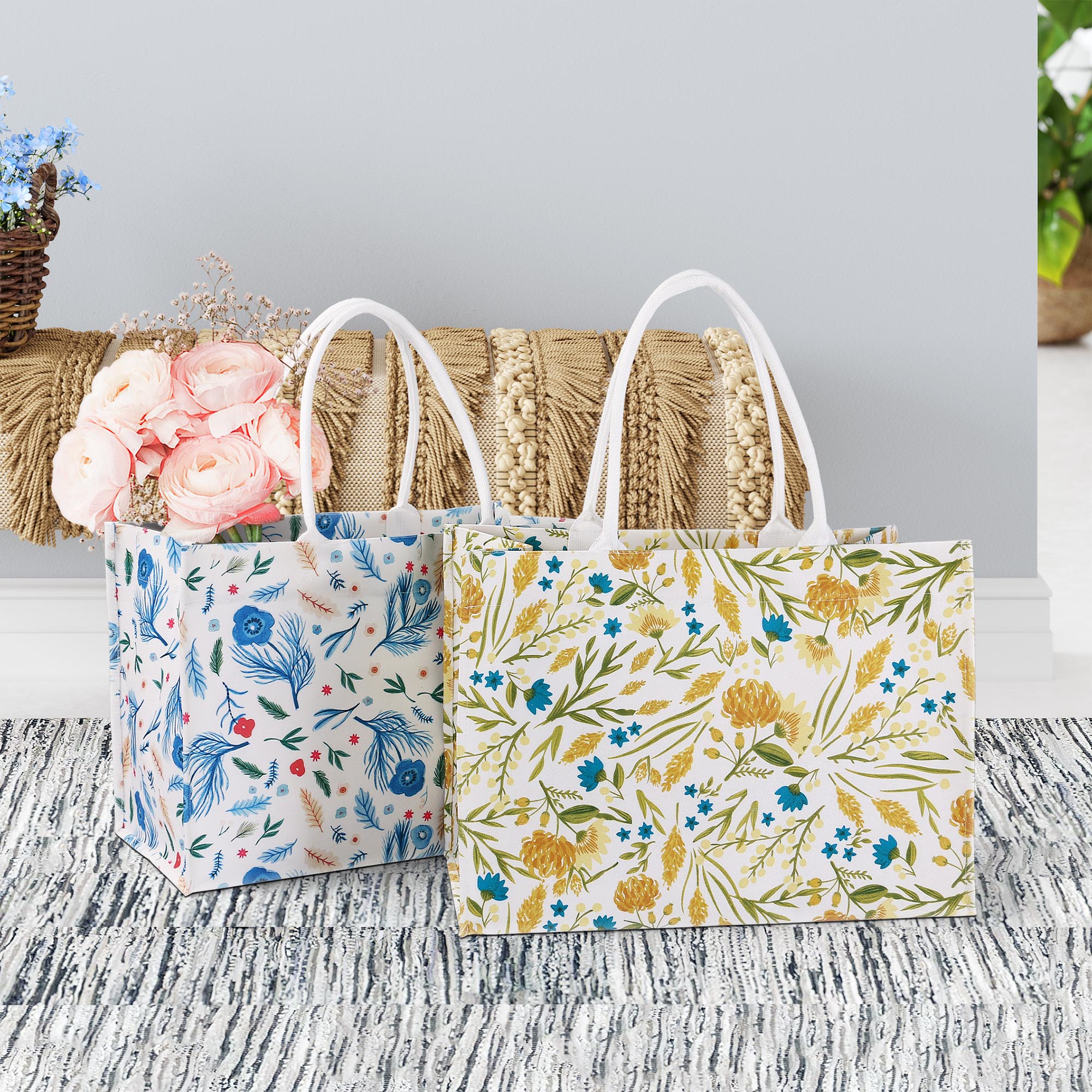 ALT Two large printed canvas tote bags with white webbing handles, one featuring a blue botanical floral print and the other a yellow floral print, with pink roses placed inside-2