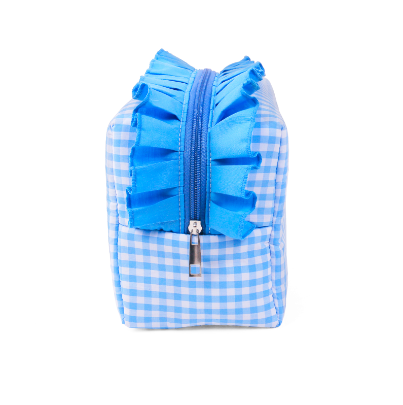ALT Front view of a blue gingham cotton cosmetic pouch featuring a decorative blue ruffle on both sides of the central zipper and a silver zipper pull.